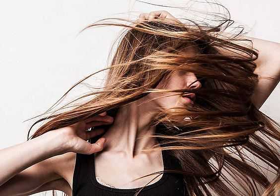 Woman dancing with hair swirling around her face, wearing a black top against a white background.