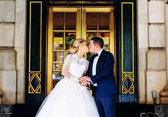 Bride and groom kissing in front of ornate building entrance.