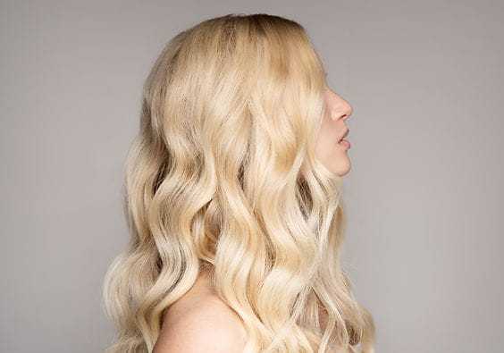 Blonde woman with long, wavy hair in profile against a neutral background.