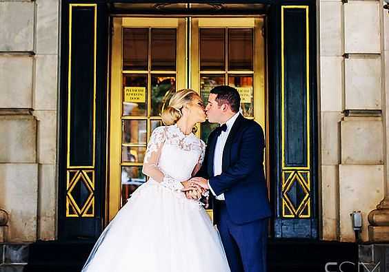 Bride and groom kissing in front of ornate building entrance.